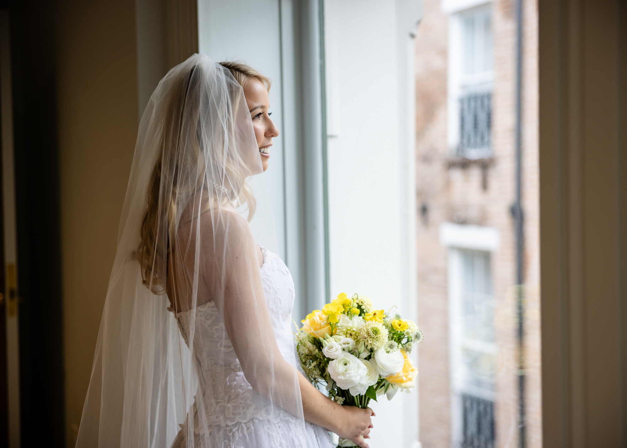 The bride holds her bouquet while looking at street below at the New Orleans Board of Trade.